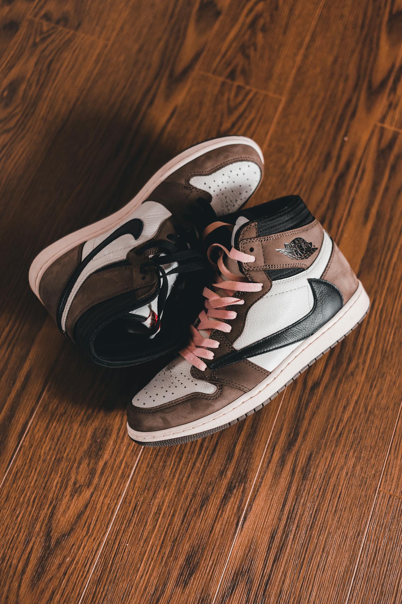 High-top Air Jordan sneakers with pink shoelaces on a wooden floor, showcasing modern footwear design.
