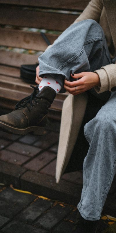 A stylish urban scene featuring a person in jeans and boots on a wooden bench adjusting their socks.
