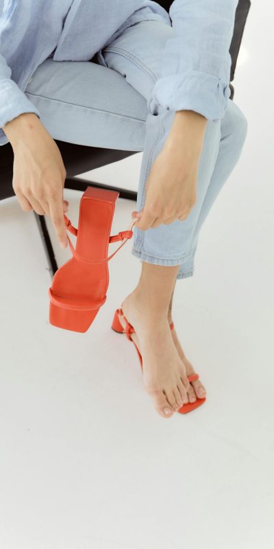 Close-up of a woman adjusting red sandals while wearing denim jeans. Fashionable and chic footwear style.